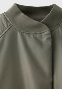 Veste vert olive avec un col en maille côtelée et un corps en tissu lisse montrée de la partie avant supérieure.