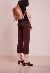 Henkilö pukeutunut ruskeisiin lyhyisiin housuihin, mustaan lyhythihaiseen paitaan, ruskeisiin korkokenkiin ja ruskeaan nahkataskuun, jossa on niittejä.