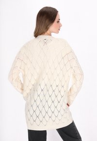 Cremefarbener Strickpullover mit einem offenen, diamantförmigen Muster. Lockerer Schnitt mit langen Ärmeln und einem gerippten Saum am unteren Ende.