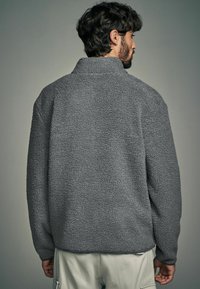 Pullover grigio in felpa con colletto alto e superficie texturizzata. Presenta maniche lunghe e una vestibilità rilassata, offrendo calore e comfort.
