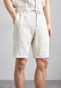 Shorts in lino beige con una vestibilità rilassata, dotati di una vita elasticizzata, tasche laterali e orlo sfiancato. Tessuto leggero e testurizzato.