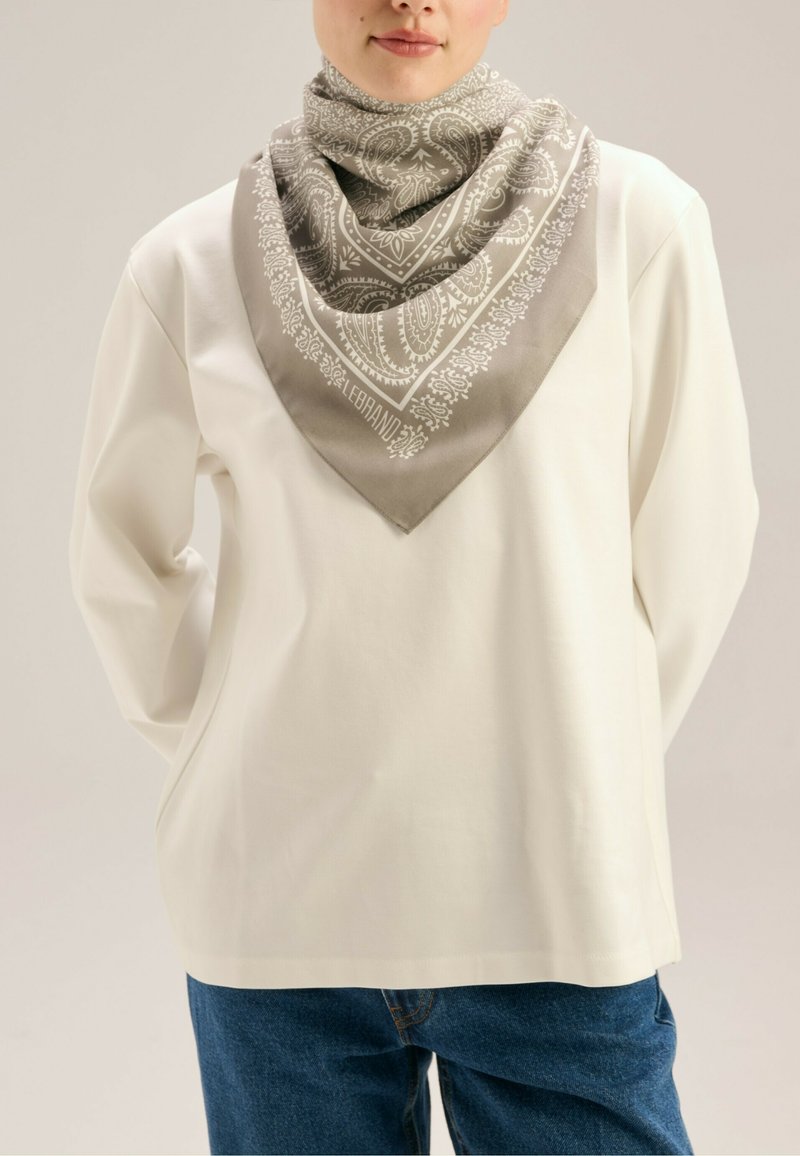 Jedwabny szal ma szary wzór paisley z białymi akcentami, w kształcie trójkąta, noszony na szyi na białej bluzce z długim rękawem.