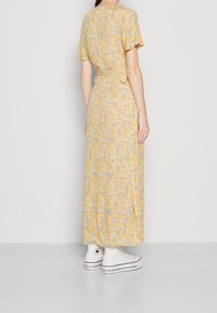 Robe maxi florale jaune à manches courtes, dotée d'une taille nouée et d'un design fluide. Assortie à des baskets en toile blanches montantes.