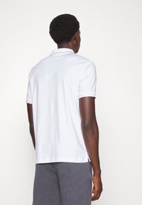 Vit pikétröja med korta ärmar och krage, med diskret branding på ärmsluten. Slät tyg, normal passform.