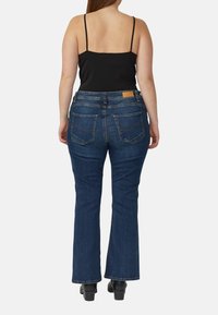 Ciemnoniebieskie spodnie dzwony z wysokim stanem, wykonane z denimu, tylne kieszenie z zakrzywionymi szwami, zestawione z czarnym topem na cienkich ramiączkach.