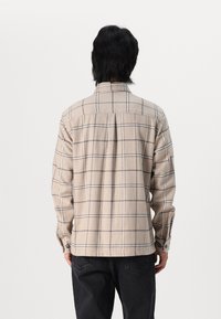 Beige flanellen overhemd met een geruit patroon in donkergrijs. Kenmerken zijn een kraag, knopenmanchetten en een relaxte pasvorm. Gestructureerde stof.
