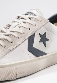 Baskets en cuir blanc avec accents en daim beige, logo étoile gris et lacets plats. Dotées d'une semelle extérieure en caoutchouc texturée et d'un design minimaliste.