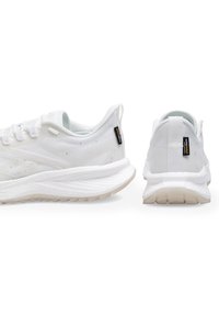 Pantofi atletici albi cu un superior din plasă texturată, guler căptușit și o talpă groasă, cu amortizare. Prezintă o etichetă cu logo pe spate.