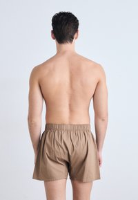 Boxeri maro cu talie elastică, realizați dintr-un material neted, prezentați din spate pe un fundal de piele dezgolită. Design simplu.