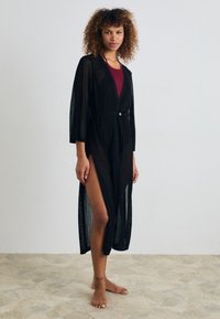 Musternik, läbipaistmatu kimono-stiilis katteväli laiade varrukatega, kinnitatud taljega ja külgmiste lõigetega. Tal on nööbikaunistus talje juures.