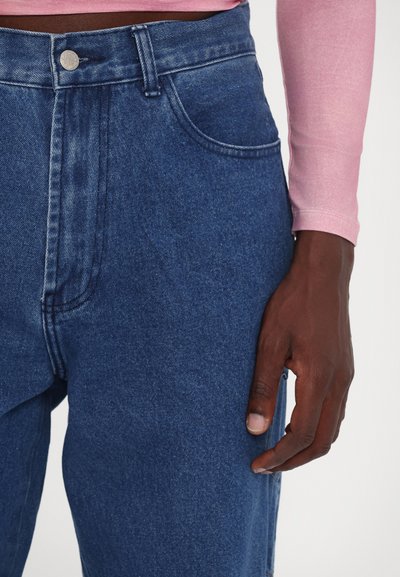 Blue denim jeans with a high waist, featuring a silver button and classic pockets. The texture is slightly faded with visible stitching.