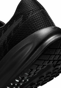 Gros plan sur l’arrière et la semelle d’une basket de sport noire montrant la tige en tissu tricoté et la semelle extérieure en caoutchouc texturé pour l’adhérence.