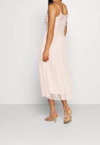 Helles rosa, ärmelloses Kleid mit einem bestickten Oberteil und einem fließenden, gefalteten Rock. Kombiniert mit leichten, offenen Sandalen.