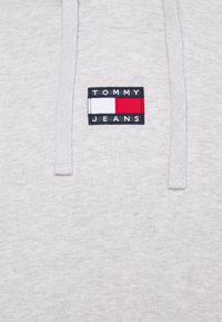 Felpa grigia con tessuto testurizzato, caratterizzata da una toppa rettangolare con il logo Tommy Jeans, con elementi rossi, bianchi e blu. Due cordini.