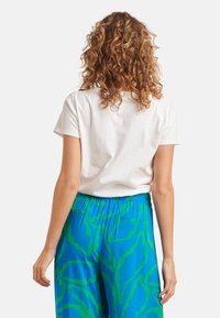Witte katoenen t-shirt met korte mouwen, gecombineerd met blauwe broek met een groen abstract patroon en een elastische tailleband.