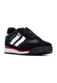 Zapatilla negra con materiales de ante y sintéticos, que presenta tres rayas blancas, un acento rojo en la suela y cordones negros texturizados.