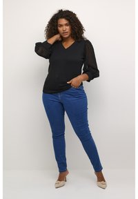 Schwarzes V-Ausschnitt-Top mit Spitzennähten, kombiniert mit blauen Slim-Fit-Jeans und beigen Absatzschuhen. Das Top hat einen glatten Stoff und Puffärmel.