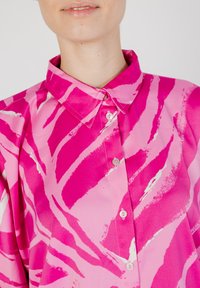 Camisa de cuello en tela de color rosa brillante con un patrón abstracto de rayas de cebra en blanco. Parte delantera con botones y pequeños botones blancos.