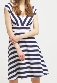 Marinblå och vit randig klänning med V-ringning, korta ärmar och en utsvängd kjol. Ränderna skapar ett geometriskt mönster. Slät tygtextur.