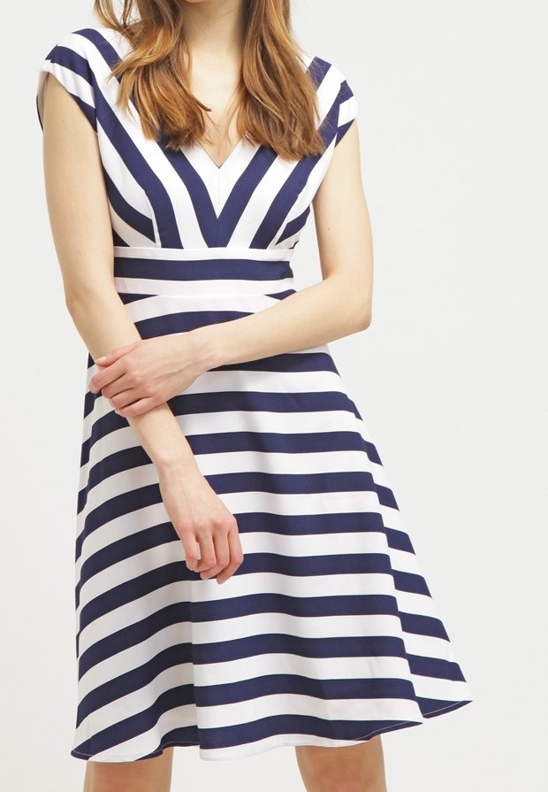 Marinblå och vit randig klänning med V-ringning, korta ärmar och en utsvängd kjol. Ränderna skapar ett geometriskt mönster. Slät tygtextur.