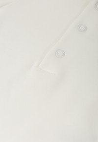 Camisa polo blanca hecha de tejido texturizado, con una tapeta de botones de colores claros y un diseño limpio y minimalista.