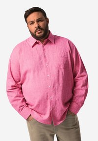 Camicia rosea con bottoni realizzata in tessuto texturizzato, caratterizzata da una tasca sul lato sinistro del petto e maniche lunghe, abbinata a pantaloni beige.