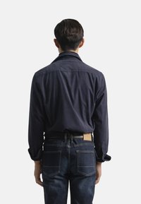 Camisa azul marino de botones con cuello extendido, mangas largas y puños doblados, combinada con jeans de mezclilla azul oscuro que tienen dos bolsillos traseros.