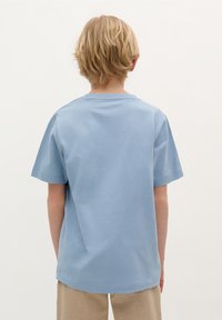 Lyseblå bomulds t-shirt med korte ærmer og rund hals, der har minimale syninger og en afslappet pasform, parret med beige bukser.
