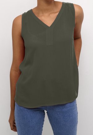 Blouse sans manches vert foncé à col en V portée avec un jean bleu par une personne debout devant un fond clair.