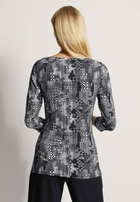 Schwarz-weißer geometrischer gemusterter Langarm-Oberteil mit rundem Ausschnitt und figurbetontem Design, das eine glatte, weiche Textur aufweist.