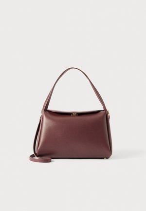 Obdélníková tmavě hnědá kožená taška s horní rukojetí, štíhlým ramenním popruhem a malým uzávěrem ve zlatém tónu na bílém pozadí.