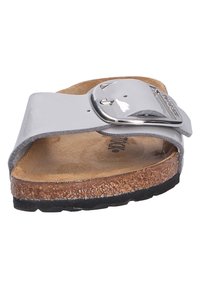 Sandale à glissière en cuir verni gris avec une grande boucle argentée, semelle en liège et semelle en caoutchouc noir texturé. Design plat pour un usage décontracté.