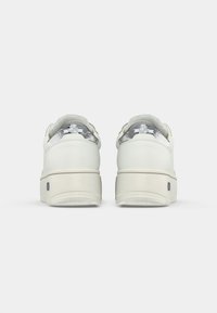 Baskets blanches en cuir lisse avec un talon surélevé, un col en chaussette grise texturée et des accents métalliques sur le panneau du talon. Semelle en caoutchouc lisse.