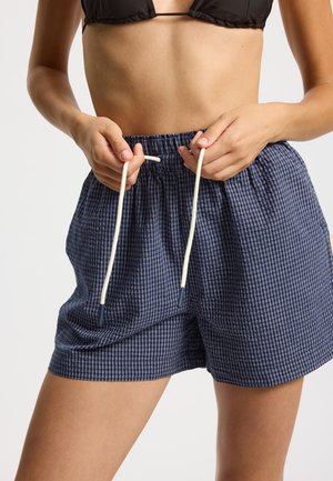 Granatowe szorty w kratę z elastycznym pasem i białymi sznurkami, cechujące się luźnym krojem i bocznymi kieszeniami. Przewiewna struktura tkaniny.