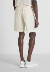 Pantaloni corti in lino color crema con vita elastica, tasche laterali e due tasche posteriori, abbinati a sneaker bianche.