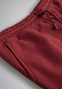 Close-up van rode trainingsbroek met elastische tailleband, trekkoord en zijzak op een gladde stoffen achtergrond.