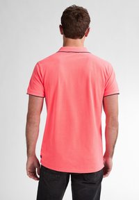 Polo shirt corail à manches courtes avec col replié, bordures contrastantes et coupe décontractée. Le tissu semble doux avec une texture subtile.