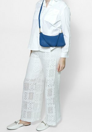 Pantalons larges en dentelle blanche à motifs associés à une chemise blanche à coupe décontractée et un petit sac crossbody bleu. Les chaussures sont des mocassins blancs.