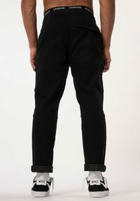 Schwarze Cargo-Hosen mit schmalem Schnitt, ausgestattet mit einer sichtbaren Gesäßtasche und umgeschlagenen Säumen. Hergestellt aus einem glatten, strapazierfähigen Stoff.