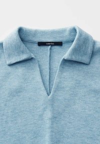 Lichtblauwe gebreide top met een gespleten V-halslijn en een zwart label met de tekst "someday" genaaid binnen de halslijn.