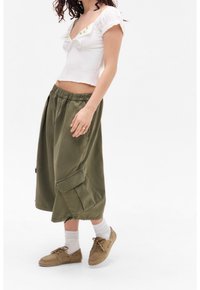 Top bianco corto con maniche a puff corte, pantaloni cargo verdi e scarpe beige. Presenta una texture smock e una vita con cordoncino.