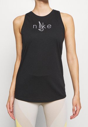 Femme portant un top sans manches noir Nike avec un logo stylisé et un legging clair avec des touches jaunes et grises.