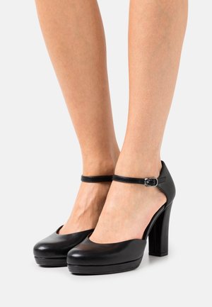 Chaussures à talons hauts noires avec une finition en cuir lisse, bout arrondi, plateforme et une bride de cheville ajustable avec une boucle argentée.