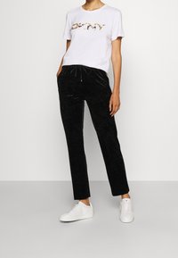 T-shirt blanc à manches courtes avec le logo 'DKNY' en motif, associé à un pantalon noir droit à texture douce et des baskets blanches.