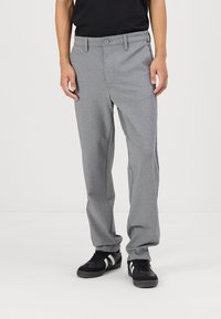 Graue, leichte Hose mit geradem Beinschnitt, flachem Bund und einem einzelnen Knopfverschluss. Getragen mit schwarzen Sneakers, die weiße Streifen aufweisen.