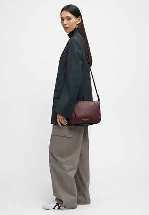 Woman wearing dark blazer, gray wide-leg cargo pants, white sneakers, carrying a burgundy leather crossbody bag over shoulder.