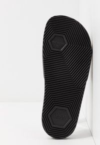 Czarna podeszwa buta z sześciokątnym wzorem, teksturowana powierzchnia i wytłoczone logo "HUGO". Projekt zawiera ukośne i poziome rowki.