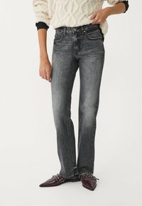 Jeans in denim nero con vestibilità a gamba dritta, caratterizzati da una texture sbiadita, cinque tasche e cuciture a contrasto. Indossati con scarpe a punta.
