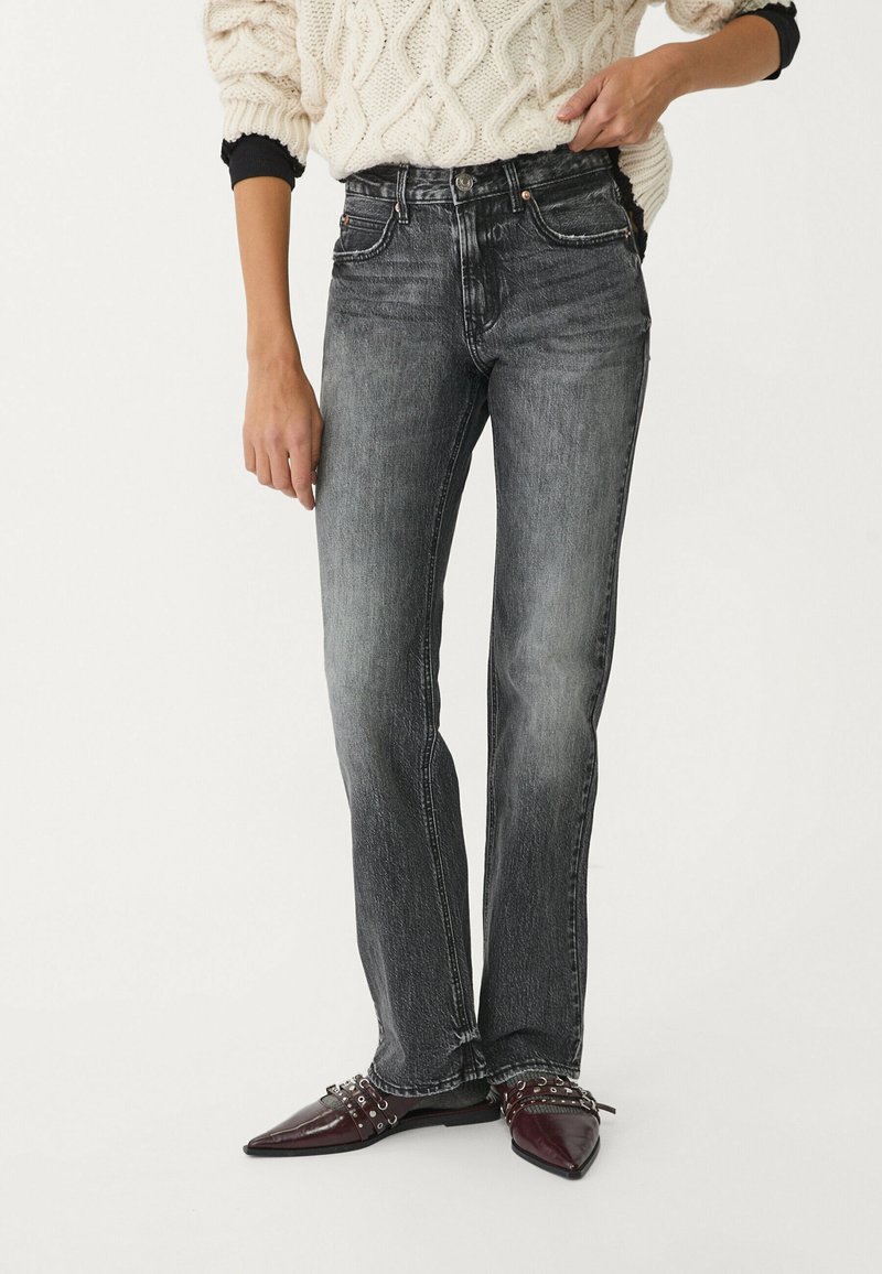 Jeans in denim nero con vestibilità a gamba dritta, caratterizzati da una texture sbiadita, cinque tasche e cuciture a contrasto. Indossati con scarpe a punta.