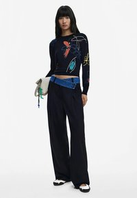 Čierny skrátený sveter s farebnou kvetinovou výšivkou, doplnený o široké tmavé nohavice a modrý rifľový opasok. Obuv má čierne a biele detaily.